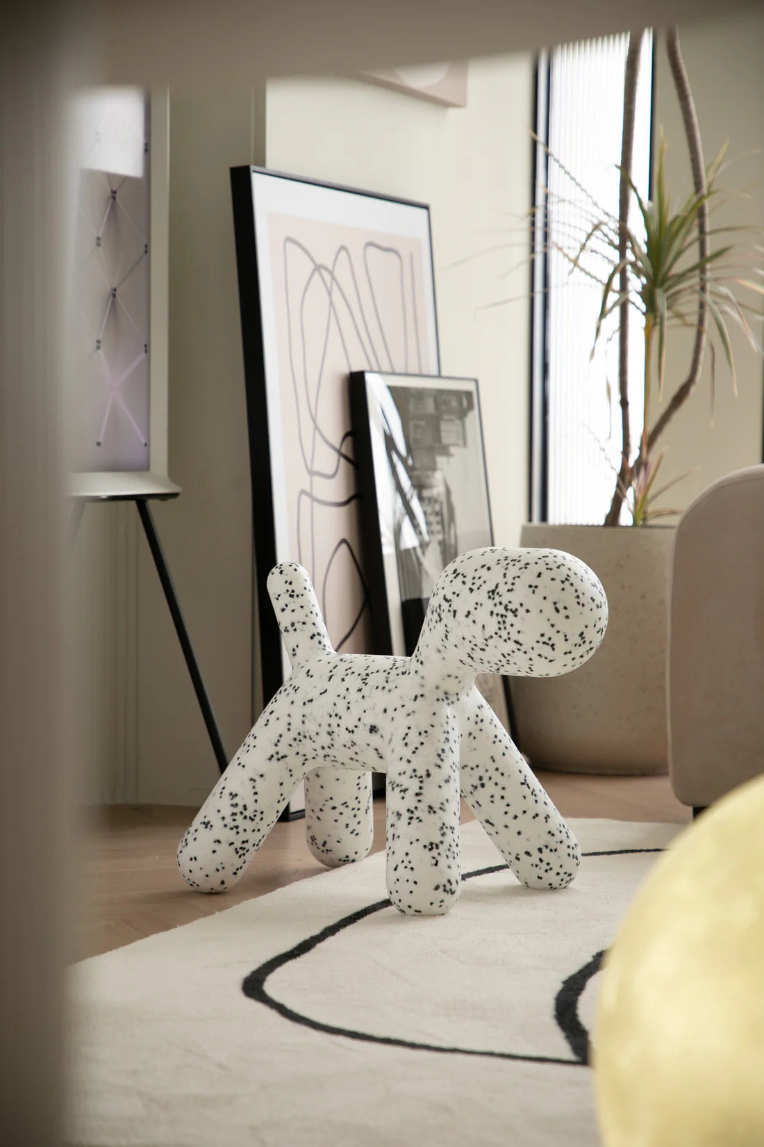 White dog-shaped plastic toddler chair with black spots  on a rug in a modern living room.