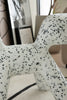White toddler chair with black speckles in a room with a mirror and framed picture on the wall.