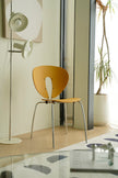 Modern chair with a yellow wooden & metal chair seat and backrest in a room with a plant and wall art.