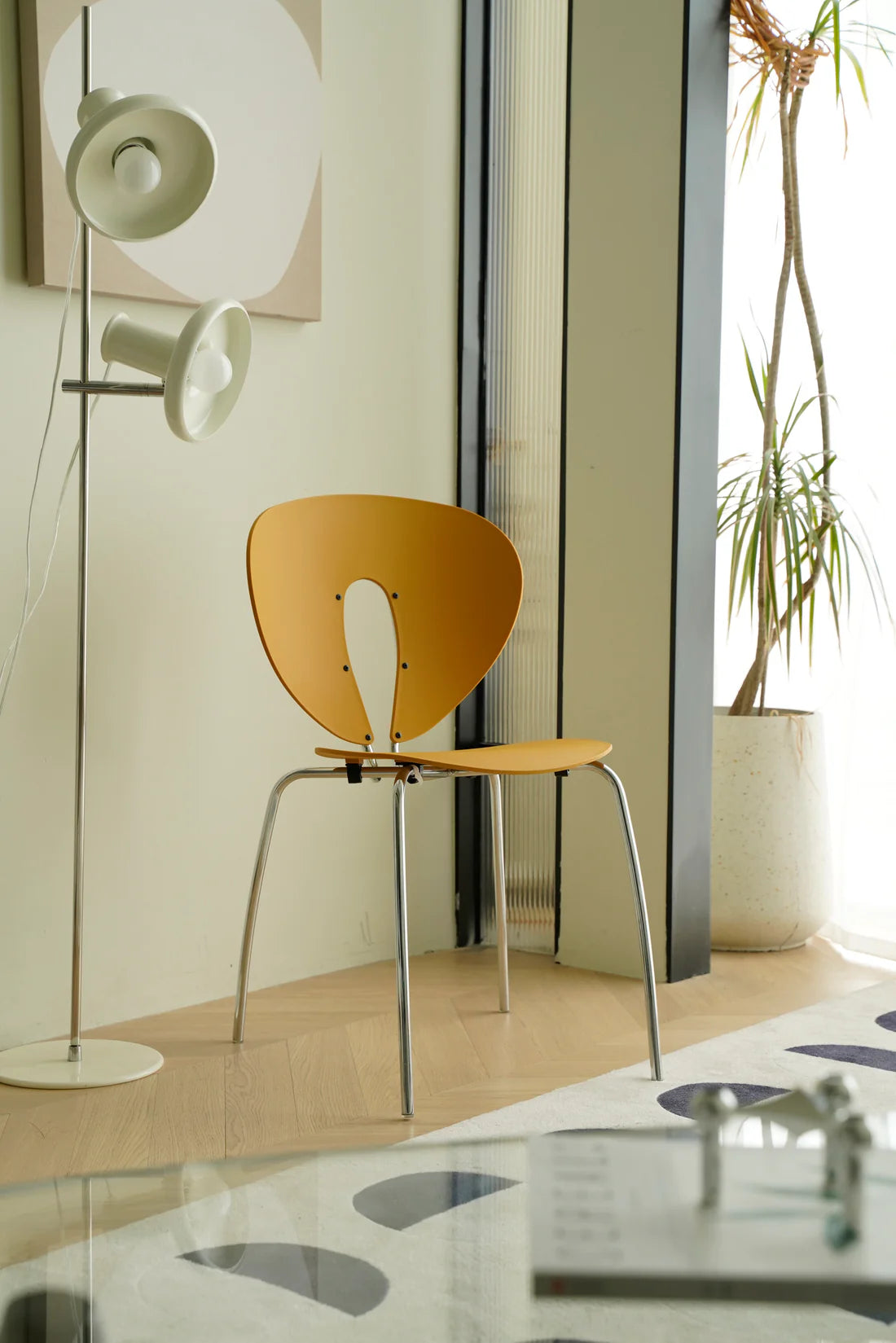 Modern chair with a yellow wooden & metal chair seat and backrest in a room with a plant and wall art.