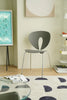 Modern gray metal chair in a room with a glass table, books, and a wall clock.