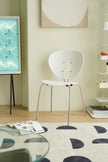 Modern white metal dining room chair in a room with a glass table, books, and a wall art piece.
