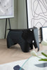 Black elephant-shaped stool in a room with a glass table and abstract wall art.