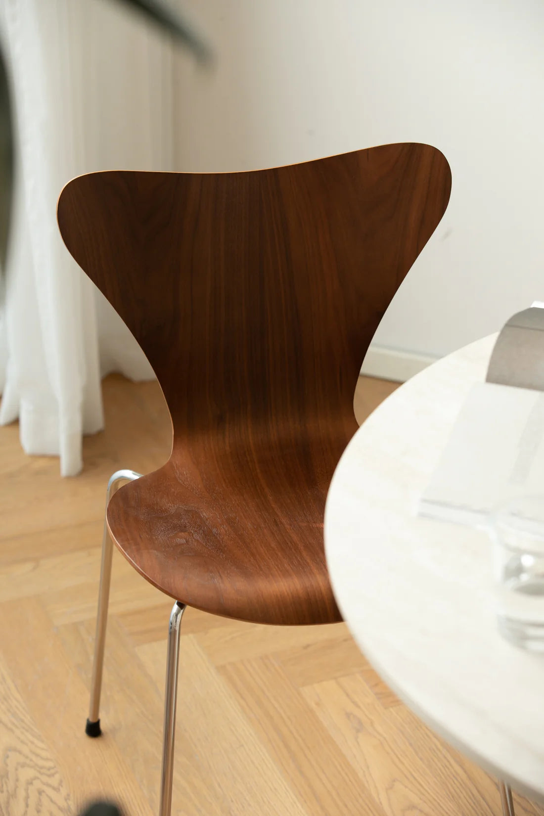 Wooden dining room chair with a white table in a room with light-colored floor and white walls