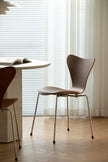 Modern wooden dining chair in a minimalistic room with light wood flooring and white curtains.