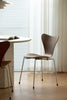 Modern wooden dining chair in a minimalistic room with light wood flooring and white curtains.