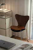 Modern dining room chair next to a metal side table with a lamp and books in a room with curtains.