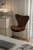 Modern dining room chair next to a metal side table with a lamp and books in a room with curtains.