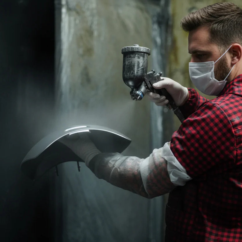 Person spray painting a surface with a mask and gloves in a dark setting
