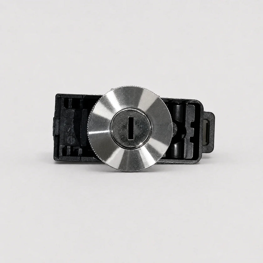 A close-up of a metallic silver key cylinder lock with a black plastic housing, shown against a plain light gray background.