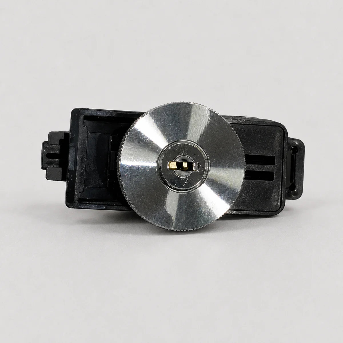 A replacement lock cylinder assembly for a door lock, featuring a circular brushed silver metal face with a black plastic housing and a small gold-colored keyway insert in the center.