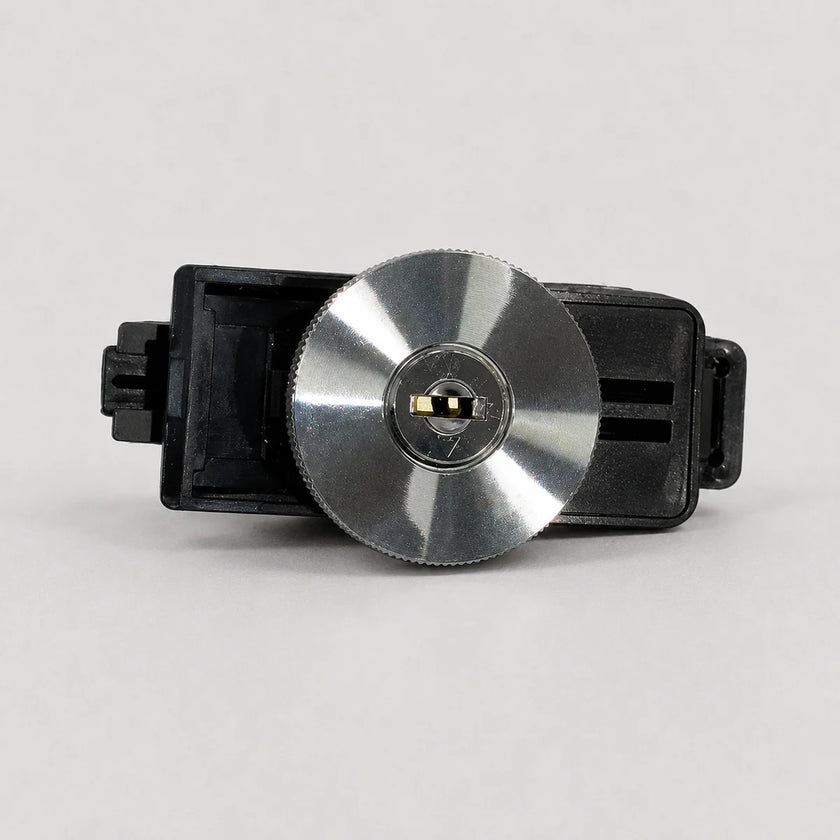A replacement lock cylinder assembly for a door lock, featuring a circular brushed silver metal face with a black plastic housing and a small gold-colored keyway insert in the center.