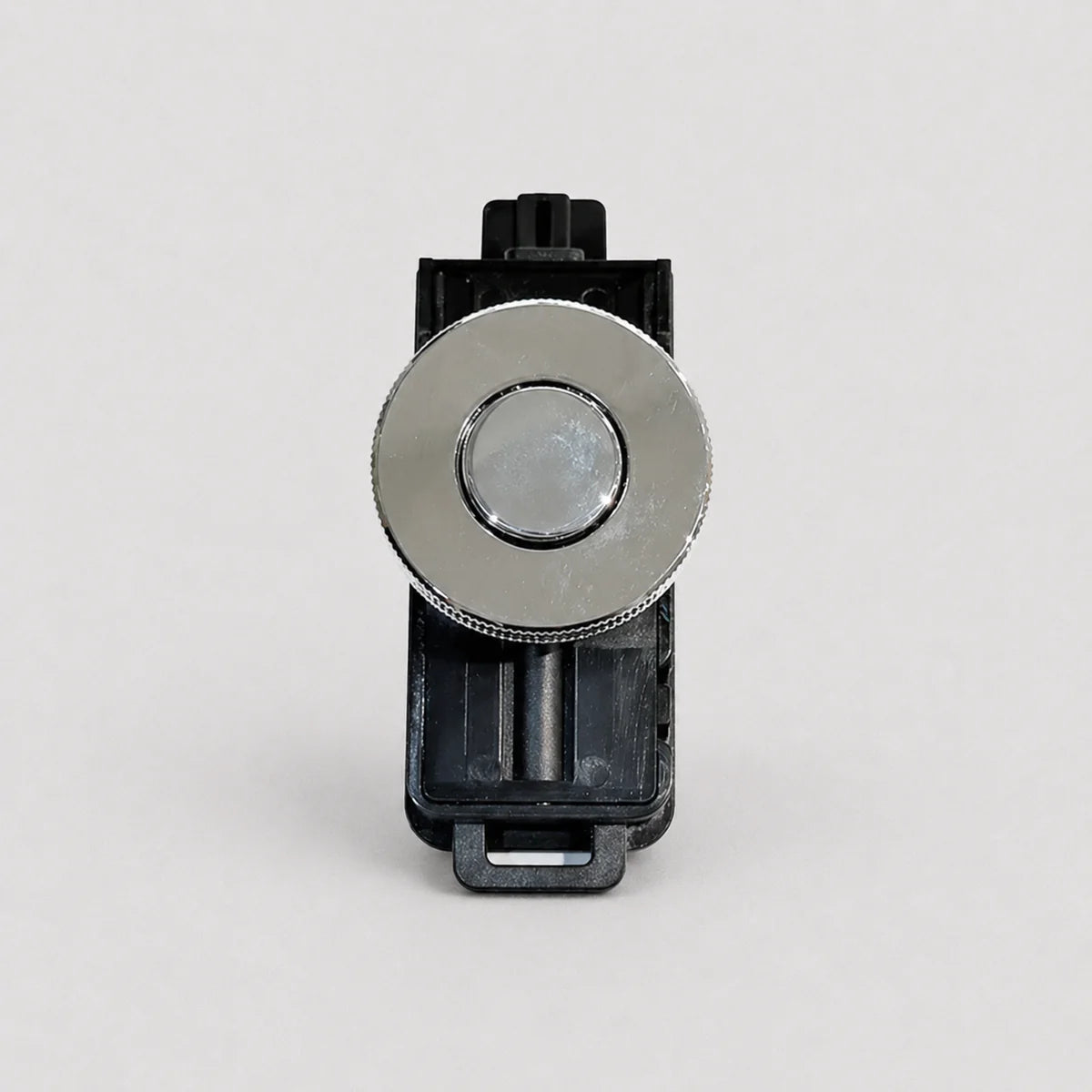 A replacement button component for a device, featuring a round silver metallic button with a textured outer ring, mounted on a black plastic housing, shot against a light gray background.
