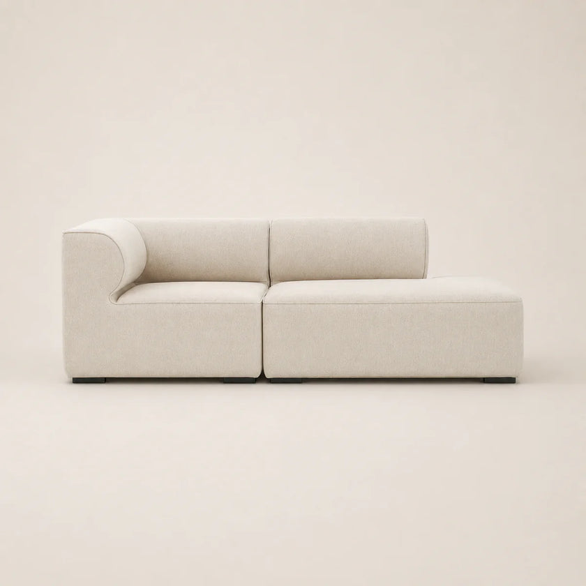 A modern modular sectional sofa in a light beige textured fabric, shown from a front-facing three-quarter angle against a solid, warm off-white background.