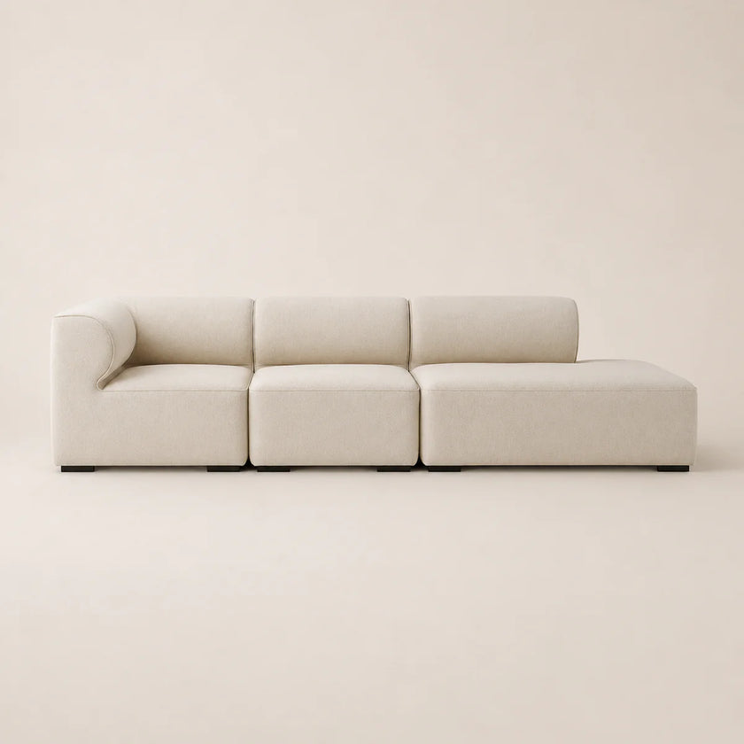 A modern modular sectional sofa upholstered in a light beige textured fabric, shown against a matching minimalist beige background.