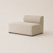 A modern low-profile modular sofa corner piece with a single chaise lounge seat, upholstered in a textured light beige fabric, shown against a solid warm beige background.