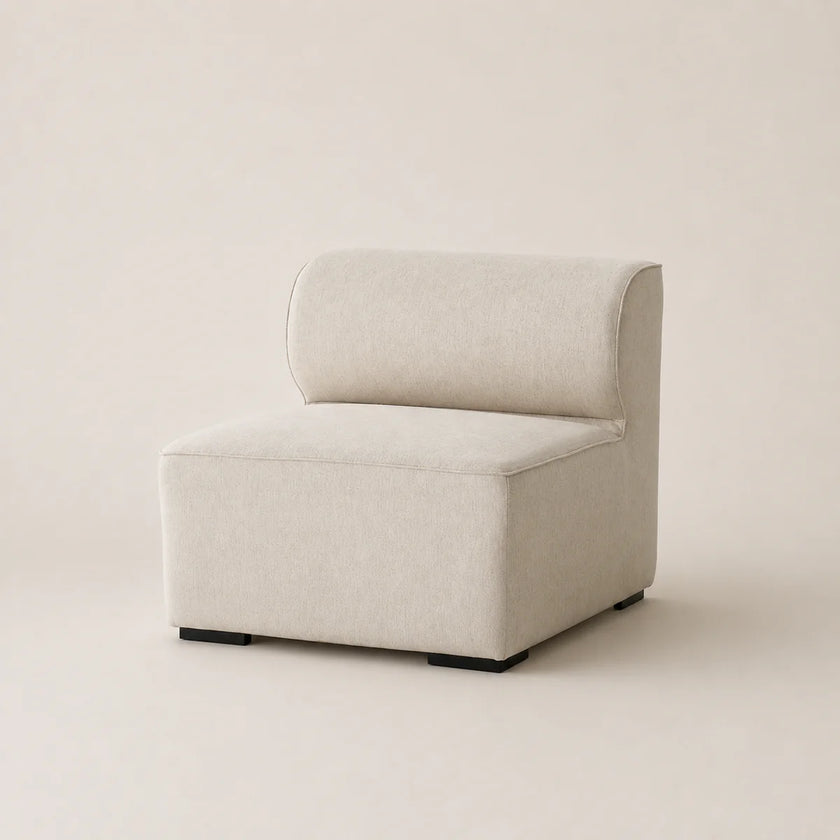 A modern low-profile accent sofa with a thick square seat and a curved backrest, upholstered in a light beige textured fabric, set against a solid warm beige background.