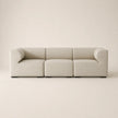 A modern three-seat modular sofa upholstered in a light beige fabric, featuring rounded armrests and a minimalist design, set against a solid warm beige background.