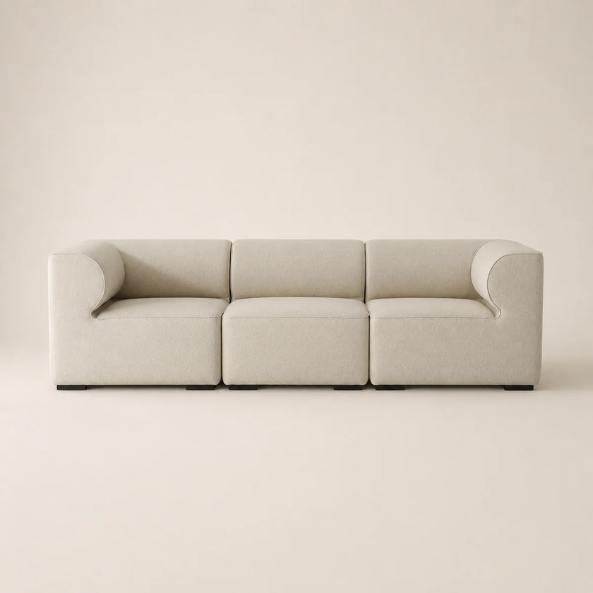 A modern three-seat modular sofa upholstered in a light beige fabric, featuring rounded armrests and a minimalist design, set against a solid warm beige background.