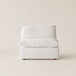 A modern low-profile accent sofa with a thick square seat and a curved backrest, upholstered in a light off-white textured fabric, set against a solid warm beige background.