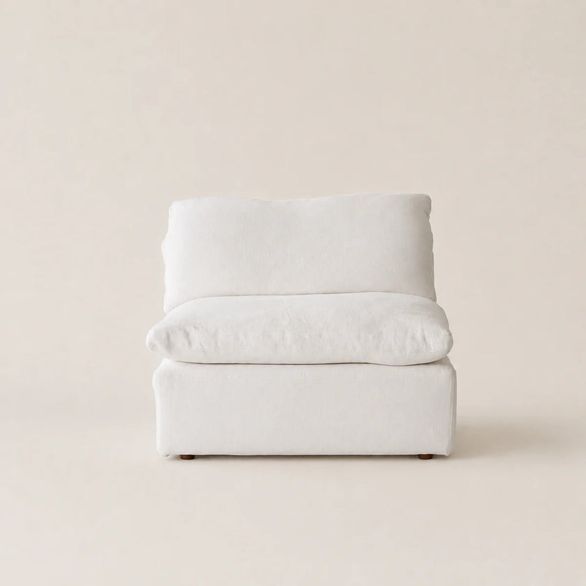 A modern low-profile accent sofa with a thick square seat and a curved backrest, upholstered in a light off-white textured fabric, set against a solid warm beige background.
