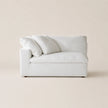 A white upholstered loveseat or armchair with three matching throw pillows, photographed against a plain warm beige studio background.