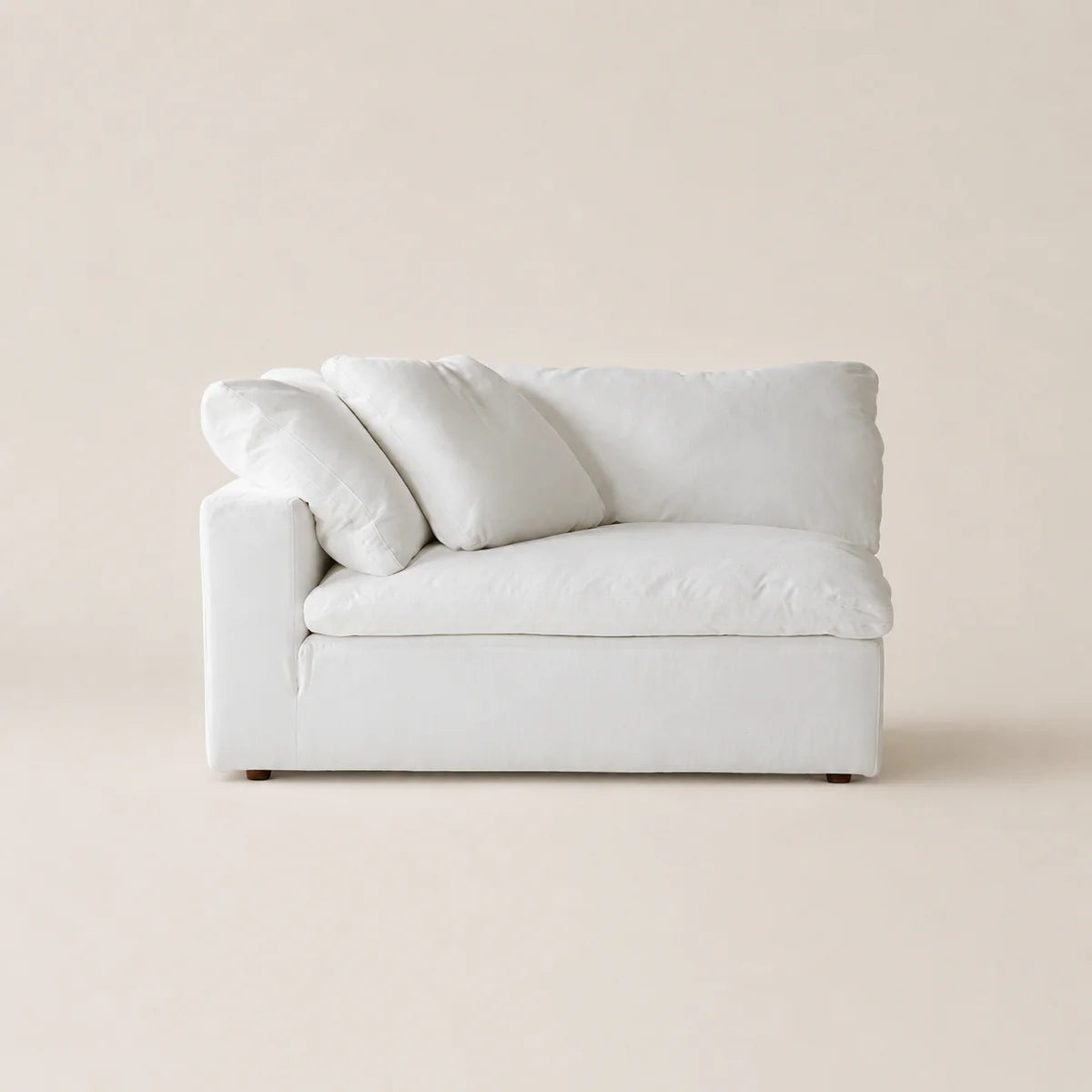 A white upholstered loveseat or armchair with three matching throw pillows, photographed against a plain warm beige studio background.