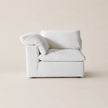 A minimalist white upholstered armchair with a matching throw pillow, set against a solid warm beige background.