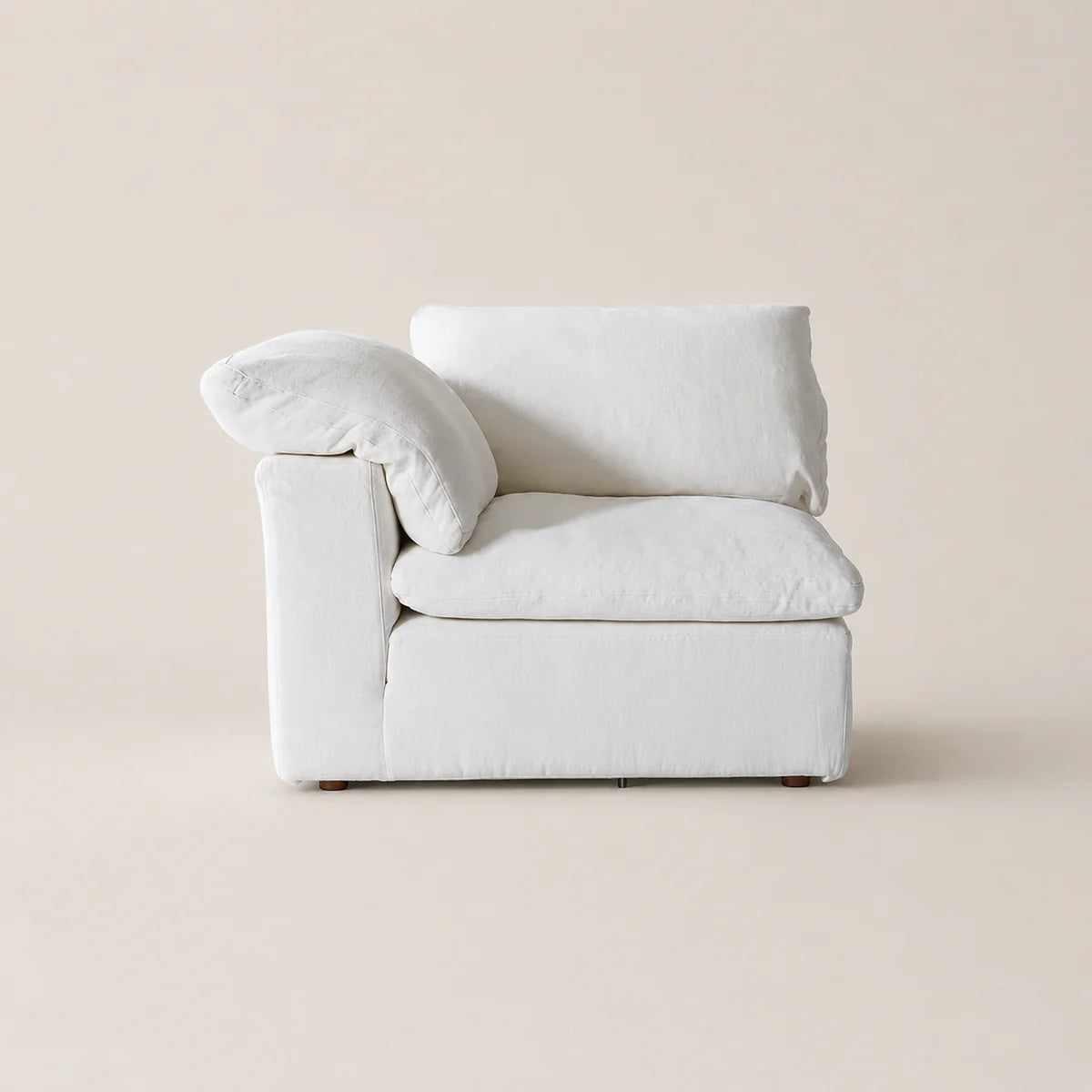 A minimalist white upholstered armchair with a matching throw pillow, set against a solid warm beige background.