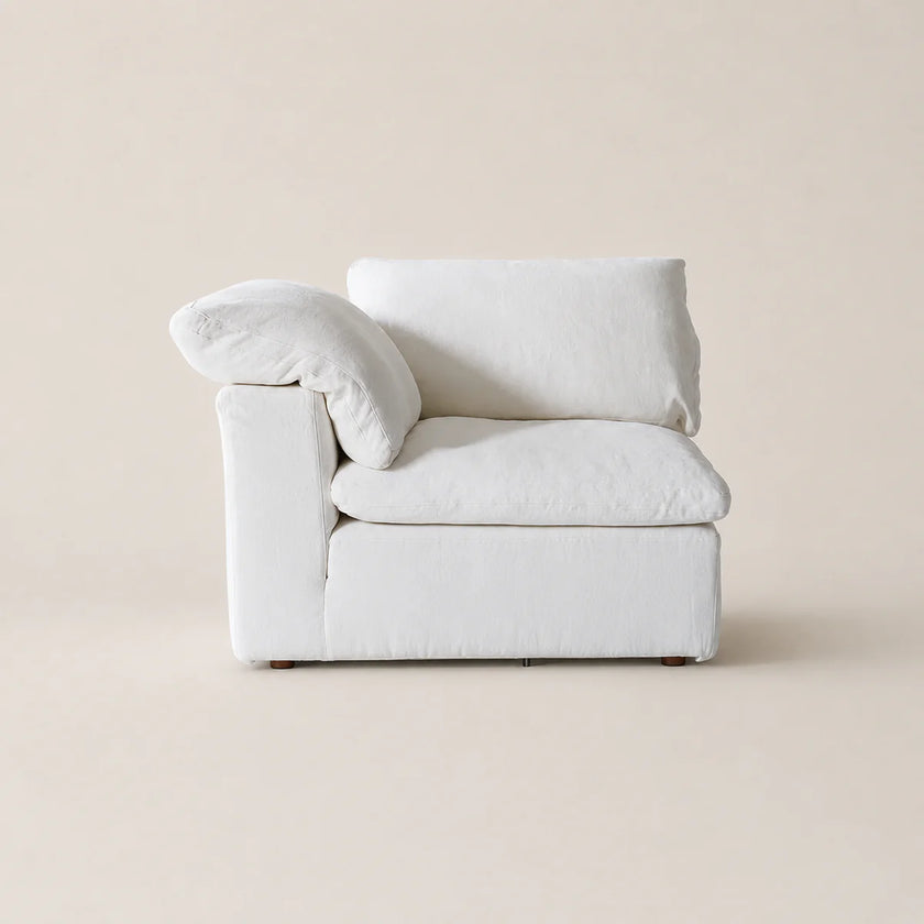 A minimalist white upholstered armchair with a matching throw pillow, set against a solid warm beige background.