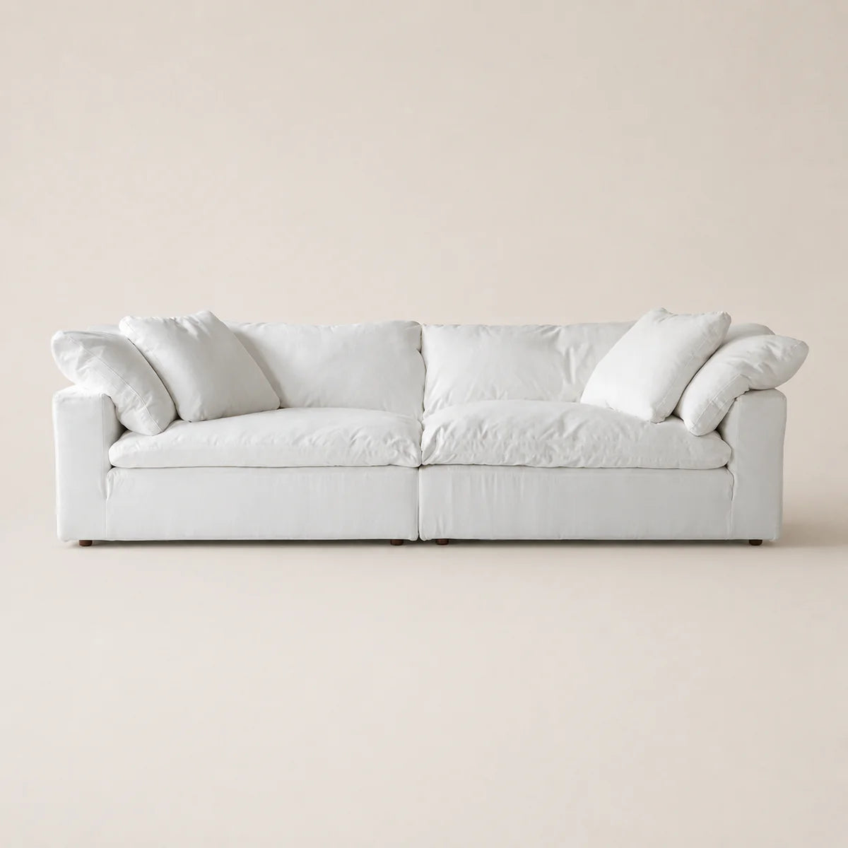 A modern low-profile white sofa with plush cushions and rolled arms, shown against a solid, warm off-white background.