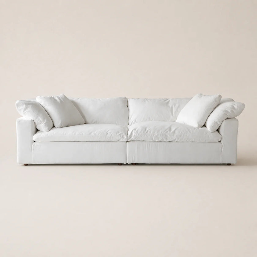 A modern low-profile white sofa with plush cushions and rolled arms, shown against a solid, warm off-white background.