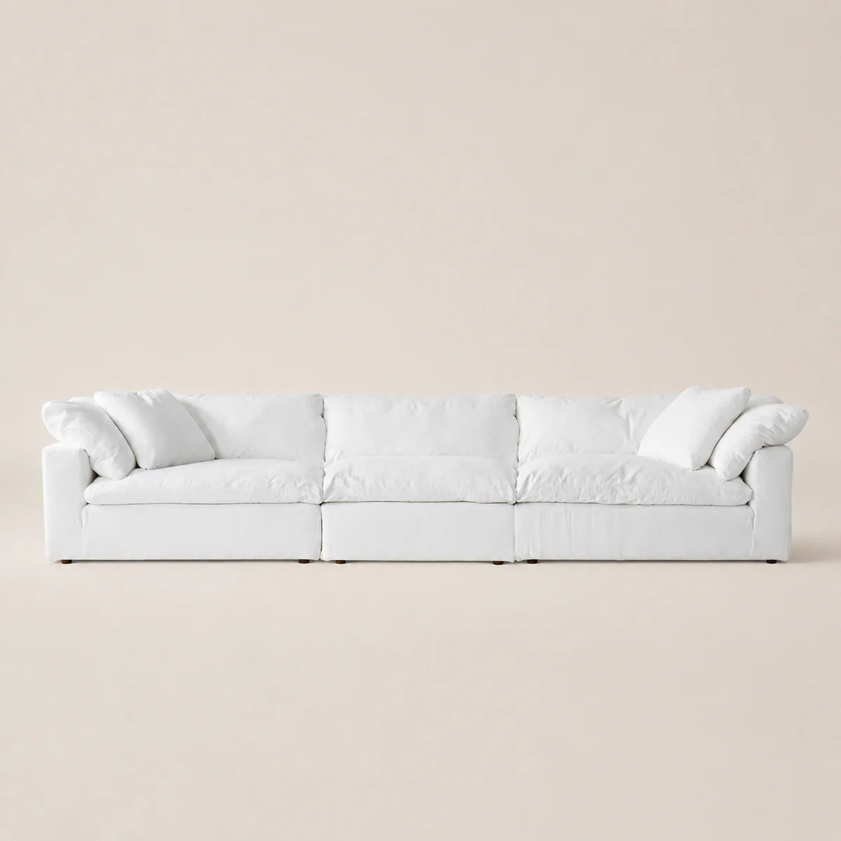 A modern white modular sofa with plush cushions and rolled arms, set against a minimalist beige background.