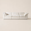 A modern three-seat sofa upholstered in off-white fabric, featuring plush cushions and rolled arms, set against a solid, warm off-white background.