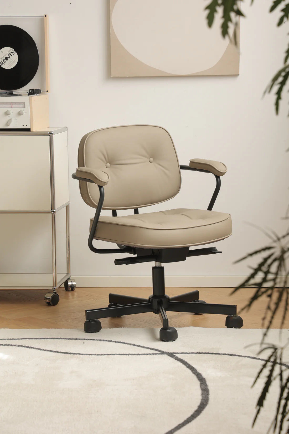 Beige office desk swivel arm chair in a room with a record player and abstract art on the wall.