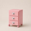 Pink jewelry box with three drawers on wheels against a beige background