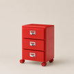 Red three-drawer filing cabinet with wheels on a beige background