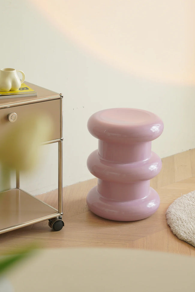 Pink plastic counter stool on a wooden floor with a light-colored wall in the background.