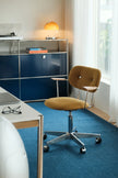 A mid-century modern office chair with a mustard yellow upholstered seat and backrest, mounted on a chrome five-star wheeled base, set in a bright home office next to a blue credenza.
