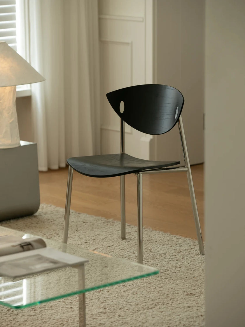 A modern black molded chair with a curved backrest and slim silver metal legs, positioned in a bright, contemporary living room setting.