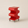 Red, wavy-shaped side table on wheels against a beige background