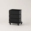 A black three-drawer storage cart with a rectangular top and four caster wheels, photographed on a clean light gray studio background.