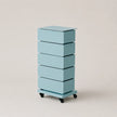 A light blue 5-drawer storage cabinet with a sliding top drawer and black caster wheels, photographed on a neutral beige background.