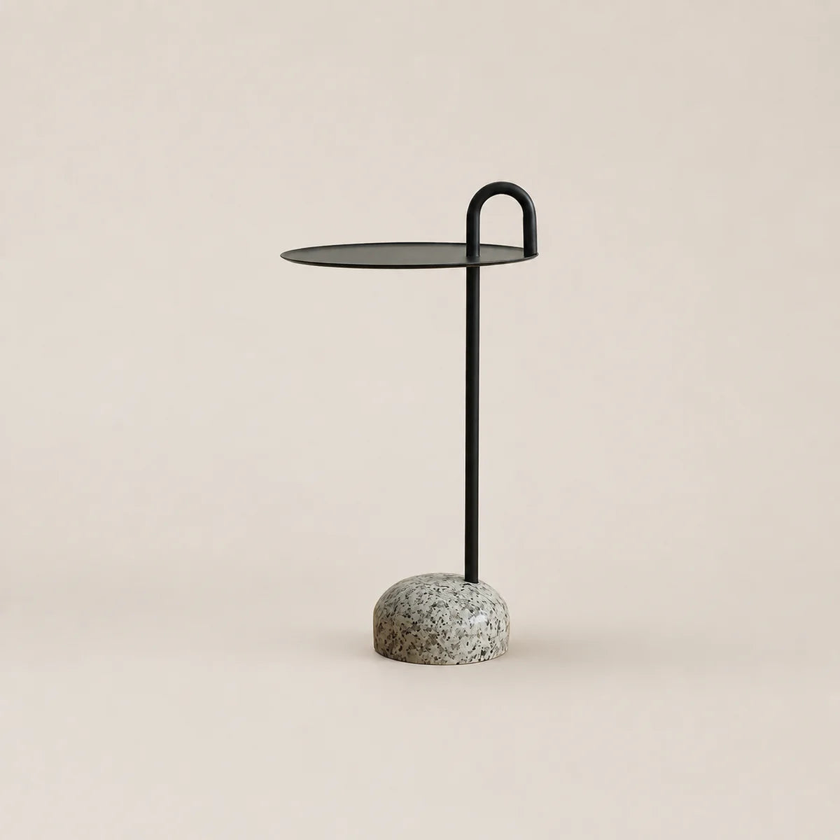 Small side table with a black metal stand and speckled gray base on a beige background