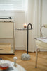 Small round black side table with a black metal frame on a wooden floor next to a chair and a window with blinds.