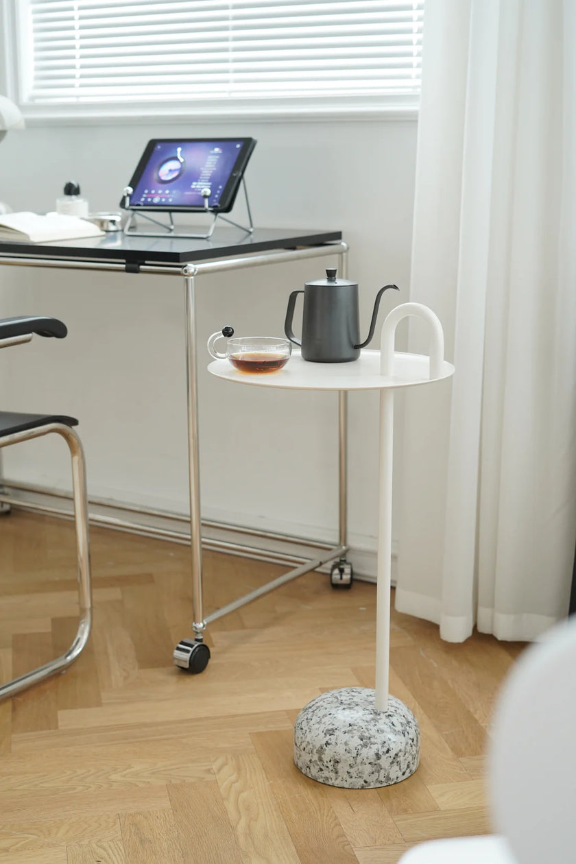 Small white round side table with a teapot and cup on a wooden floor next to a desk.
