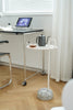 Small white round side table with a teapot and cup on a wooden floor next to a desk.