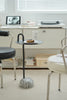Small Black round side table with a glass of water and a donut on a shelf in a room with chairs and a computer.
