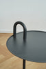 Modern black side table with curved handle on a wooden floor.