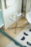 Small glass bed side table with a white mug and books on a wooden floor.
